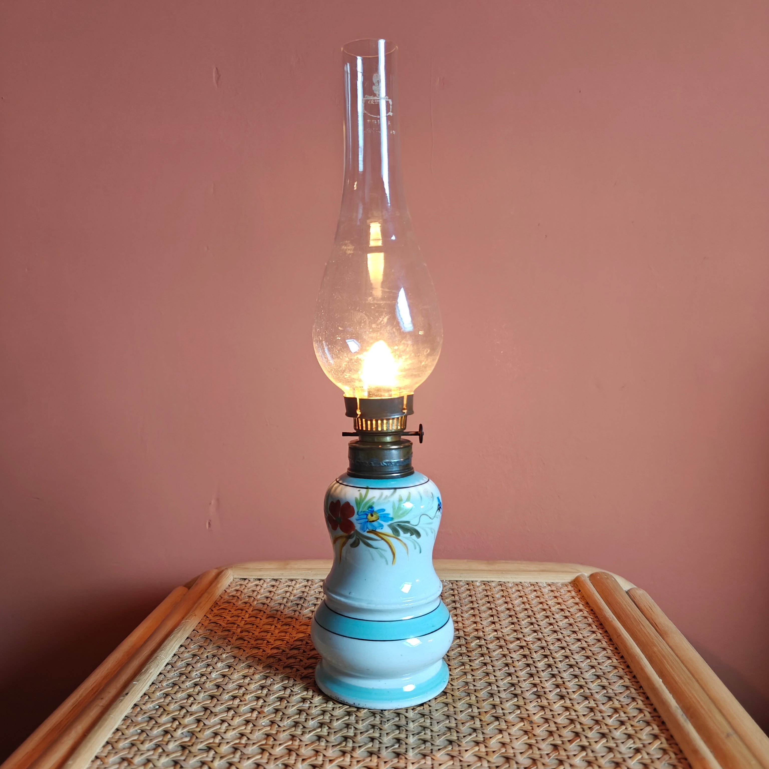Vintage Porcelain Oil Lamp – Hand-Painted with Wiener Flachbrenner Burner glowing softly on woven table surface