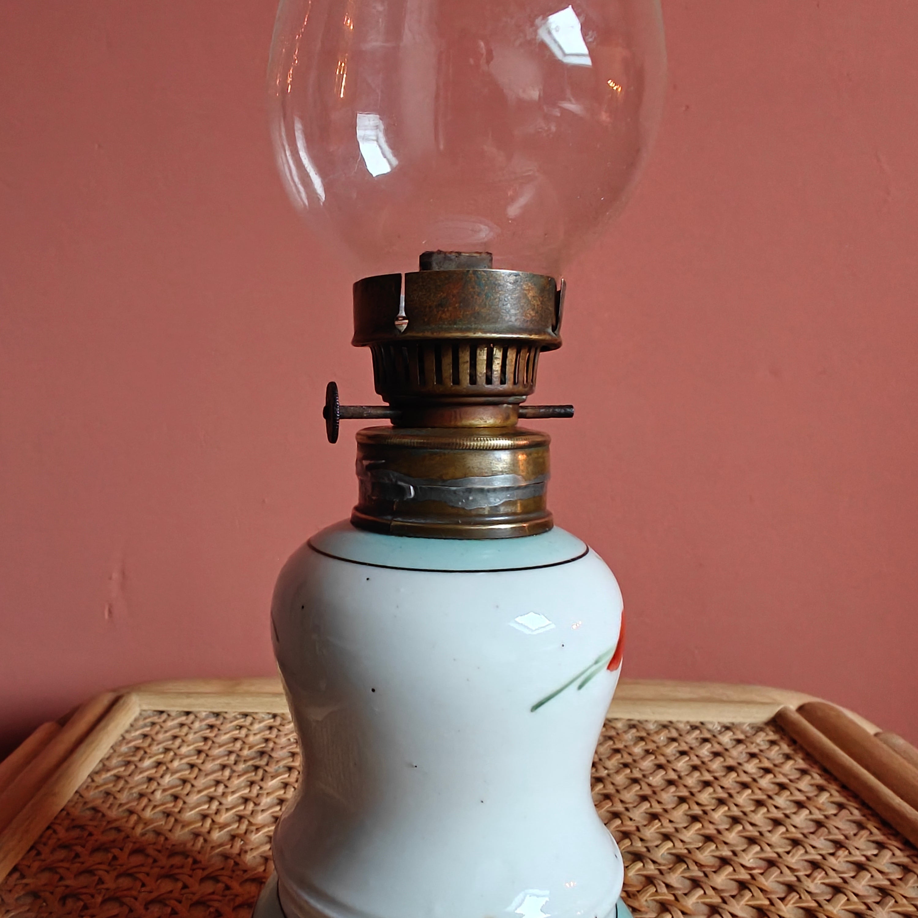 Vintage Porcelain Oil Lamp – Hand-Painted with Wiener Flachbrenner Burner on wicker surface against coral wall background