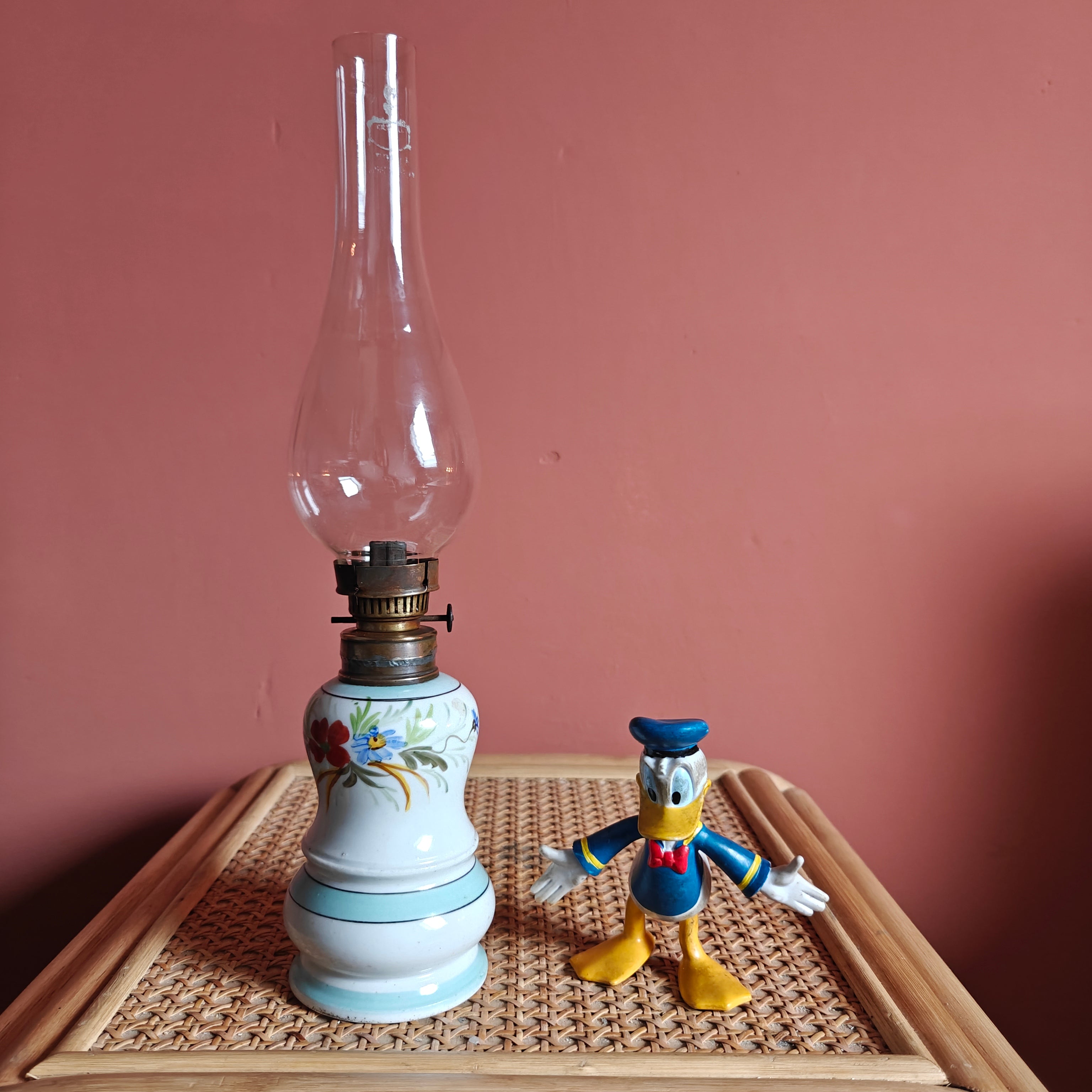 Vintage Porcelain Oil Lamp – Hand-Painted with Wiener Flachbrenner Burner displayed on wicker table beside a small figurine.
