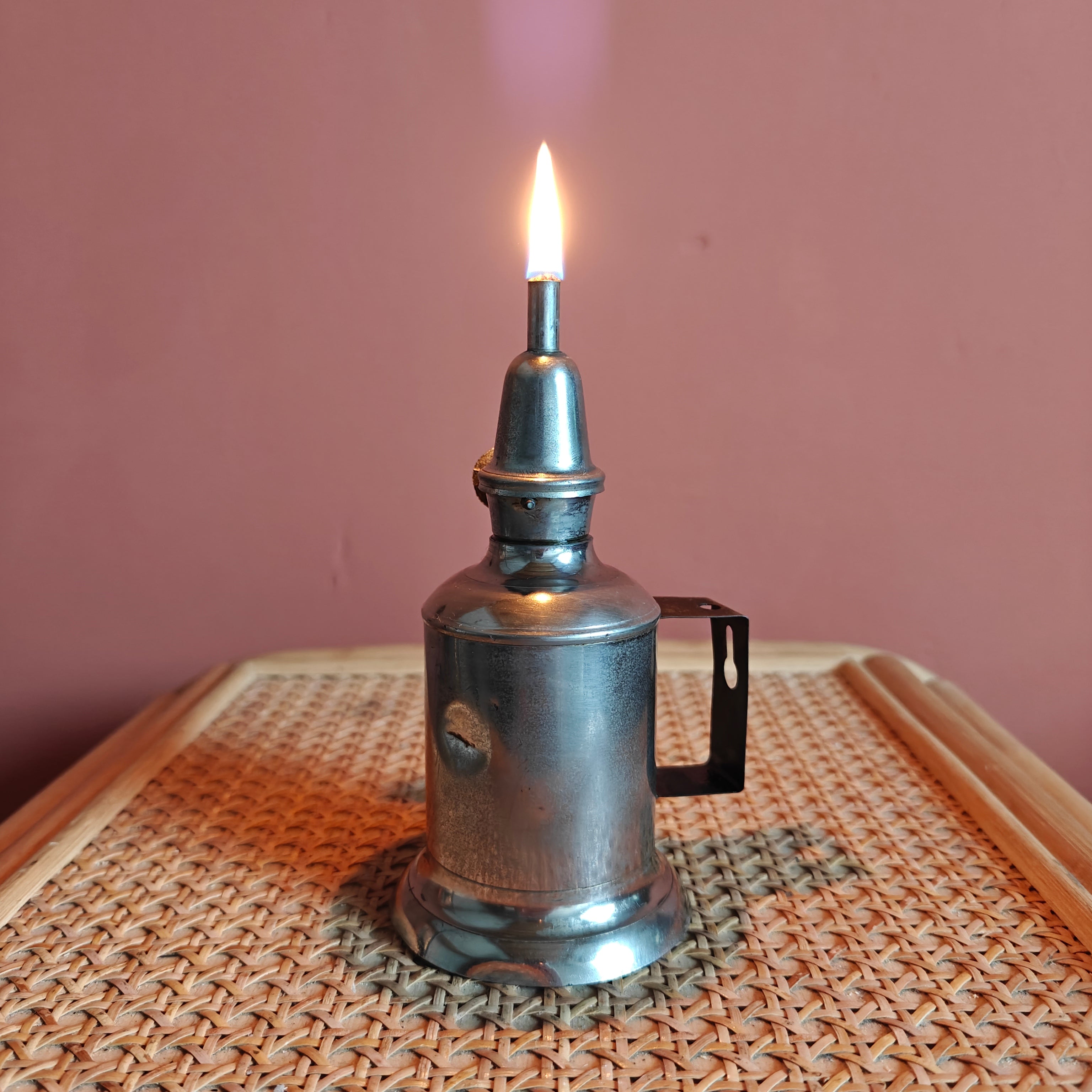 Vintage French Oil Lamp – Pigeon Style with T.F. Déposé Burner (17 cm) lit on woven surface against pink wall