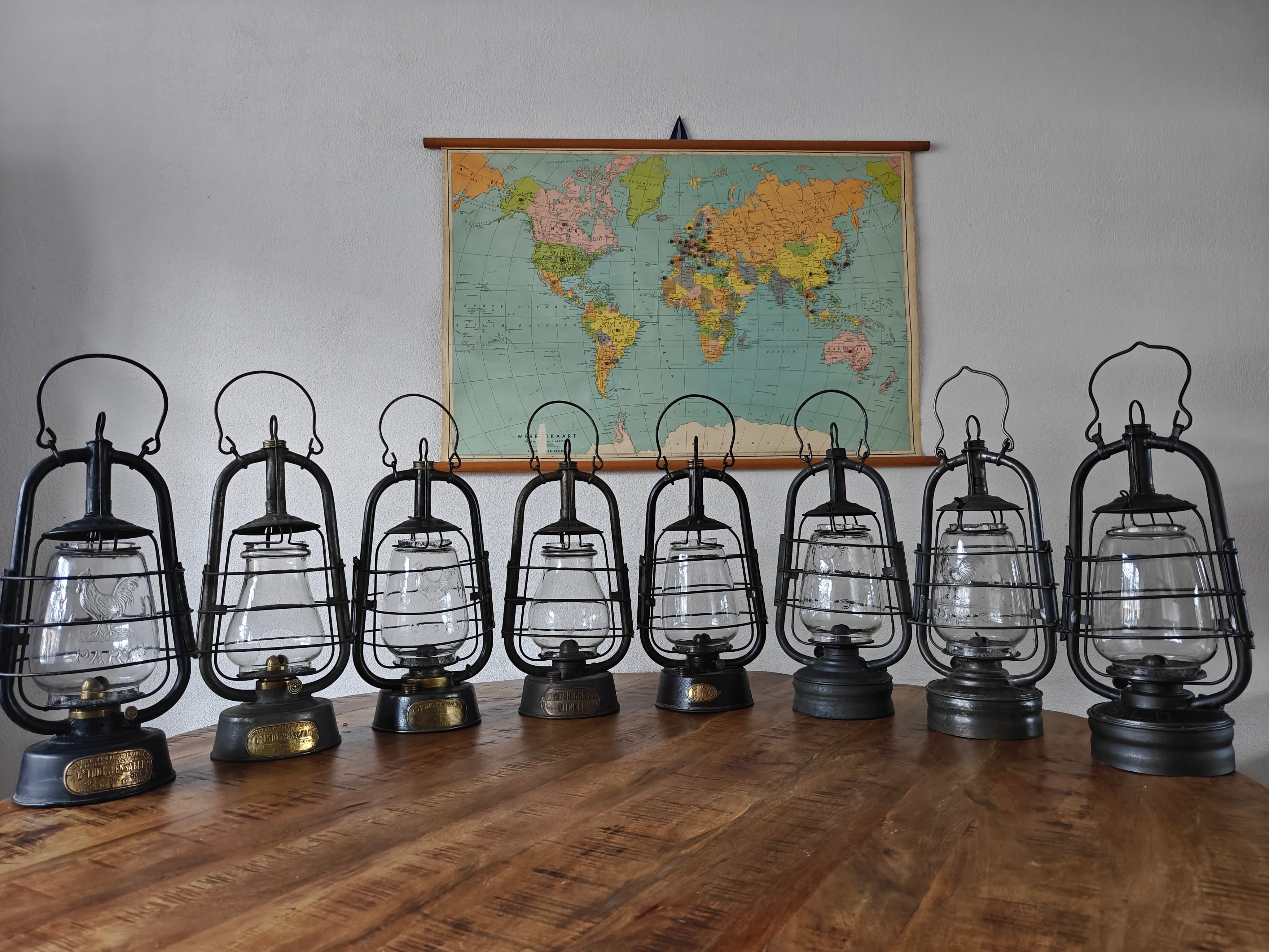 Row of black Dresco oil lamps with glass chimneys displayed on a wooden surface in front of a world map