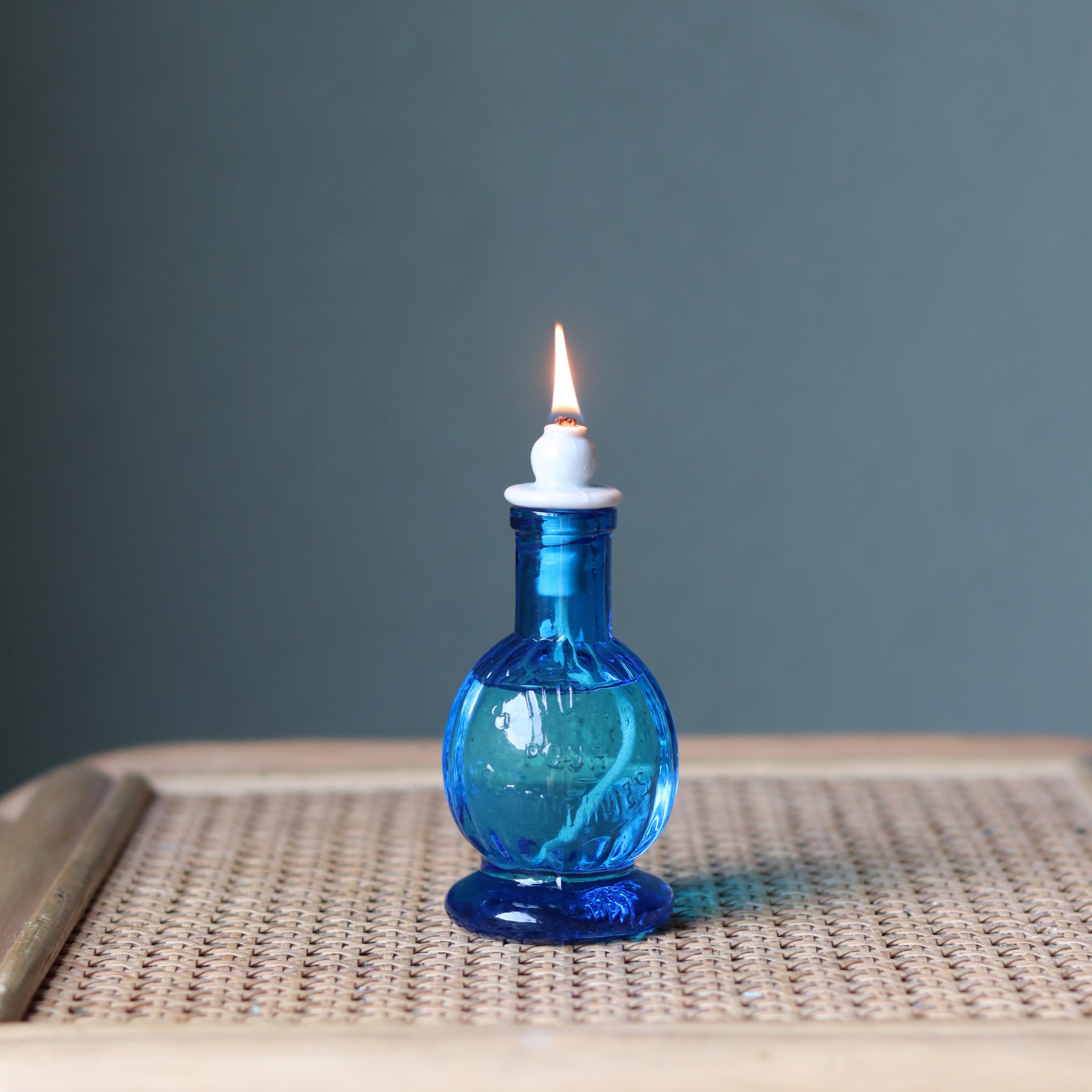 Rare Vintage French Oil Lamp – Blue Glass Bedside Nightlight (1930s–1950s) with lit flame on wicker surface