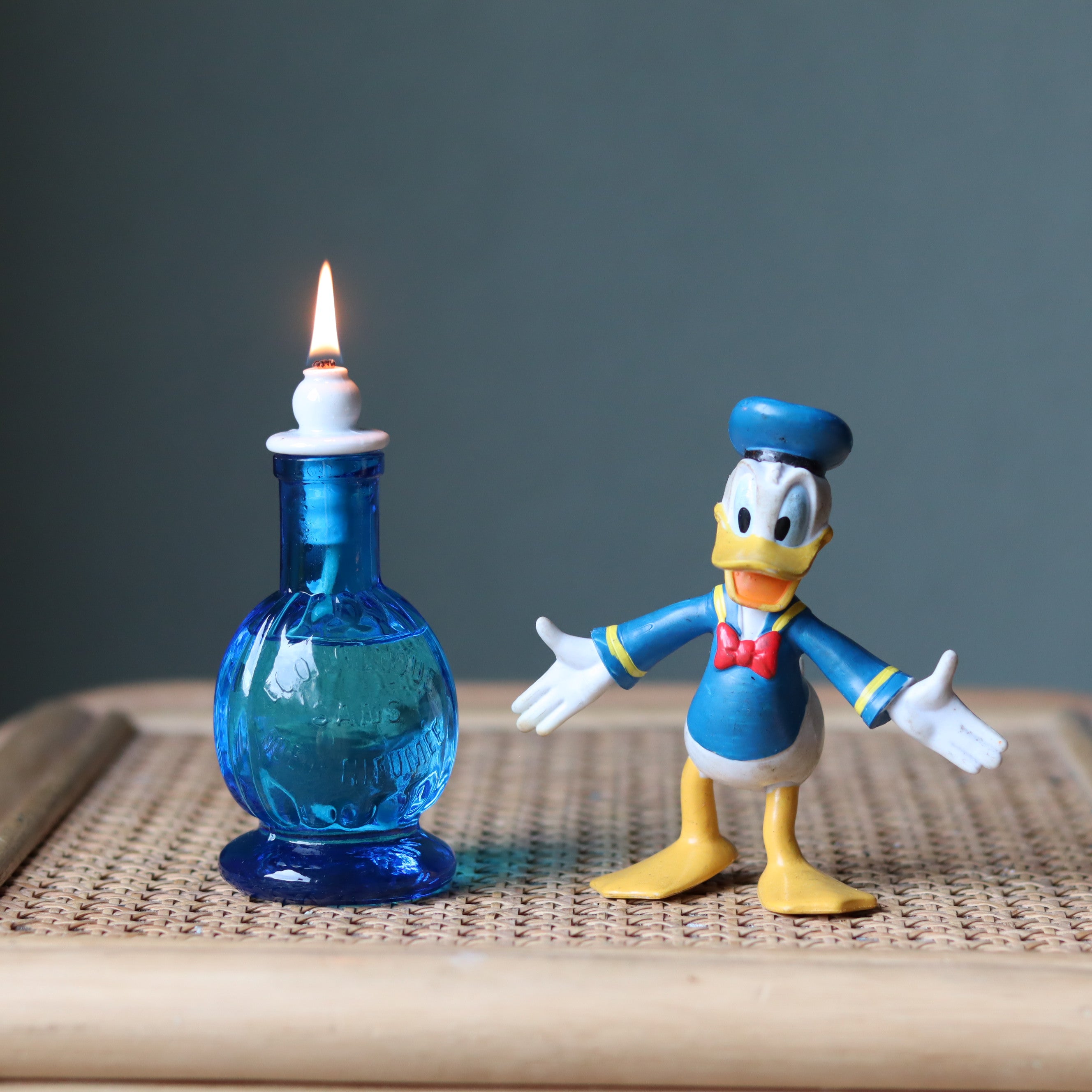 Rare Vintage French Oil Lamp – Blue Glass Bedside Nightlight (1930s–1950s) lit with a bright flame on a wicker surface