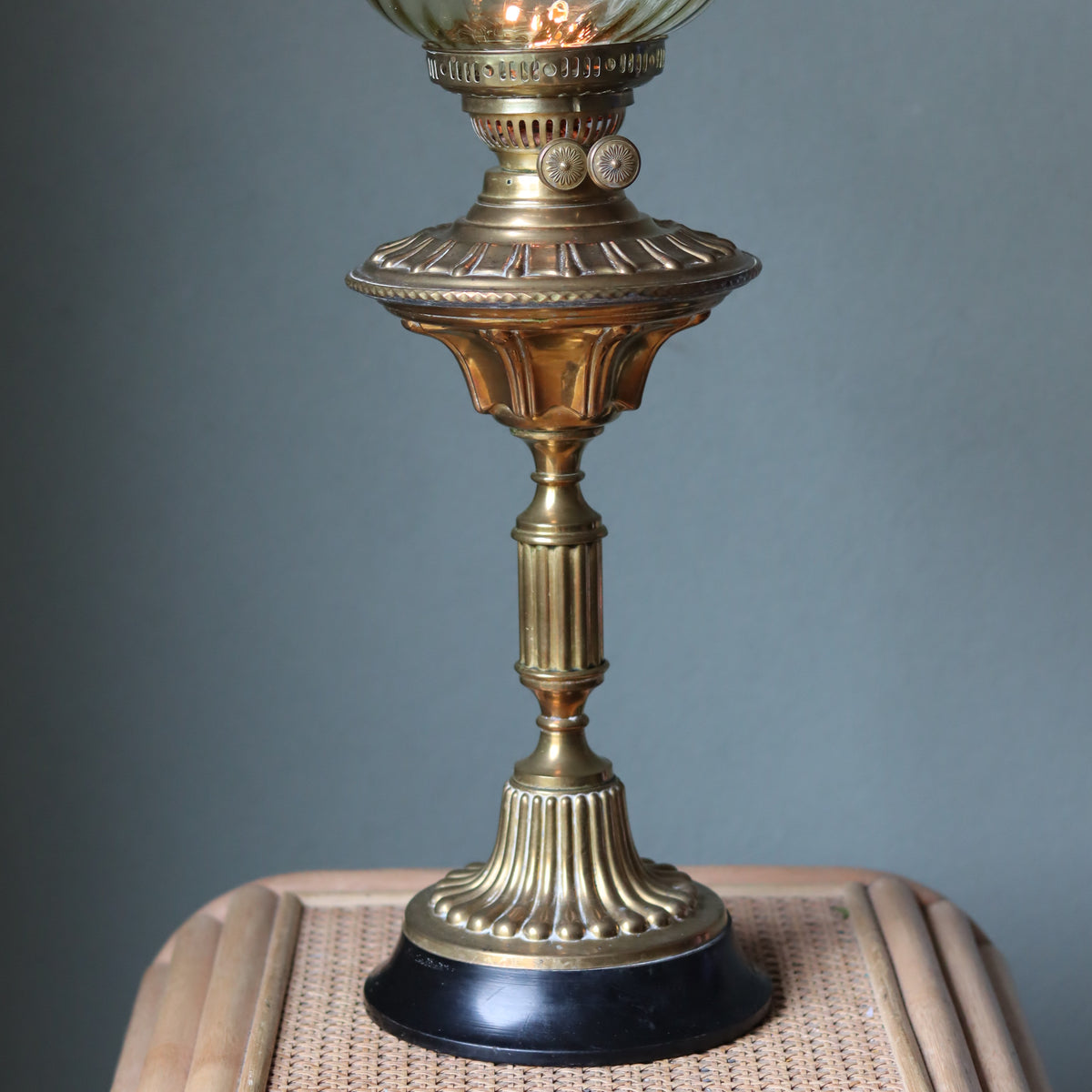 Vintage Brass Oil Lamp – Duplex Double Wick Burner – Yellow Glass Shade – 1950s–1970s standing on a wicker surface against a gray background