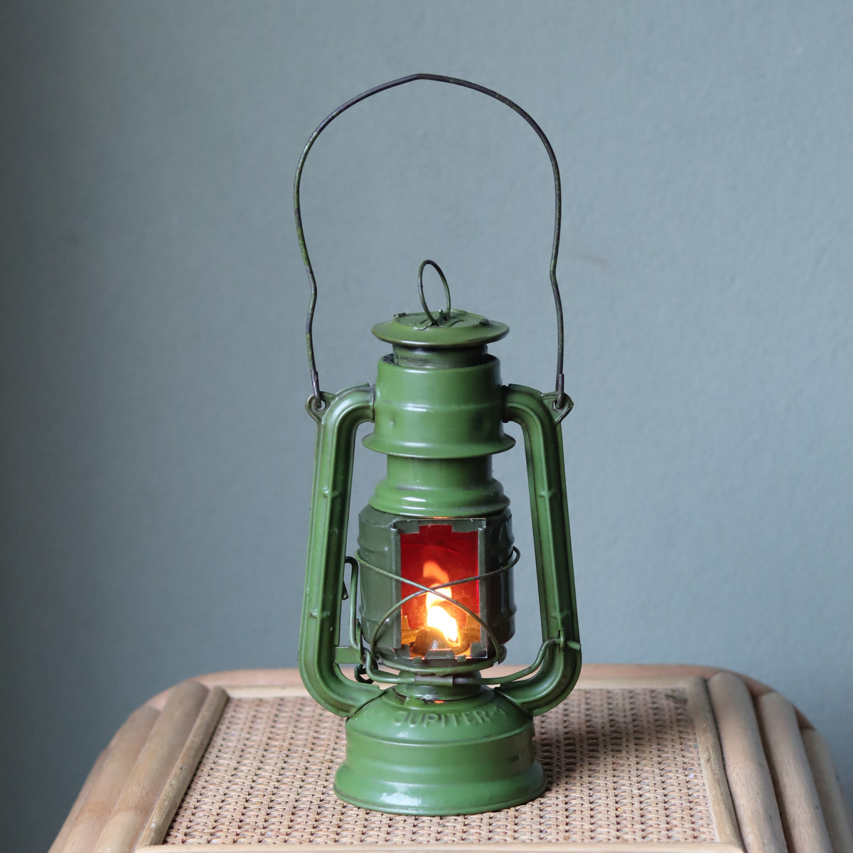 Rare Vintage Jupiter-1 Green Hurricane Lantern – Unique Flat Glass Holder with Red & Clear Panels oil lamp lit on woven surface