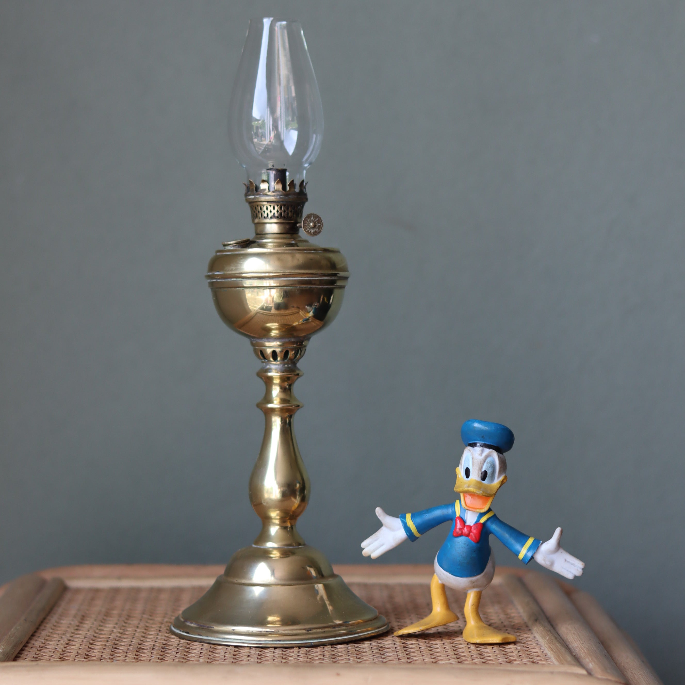 Rare Antique Oil Lamp with Unique Hollow Wick – Elegant Brass Design (c.1900–1930) beside a Donald Duck figure on a woven surface