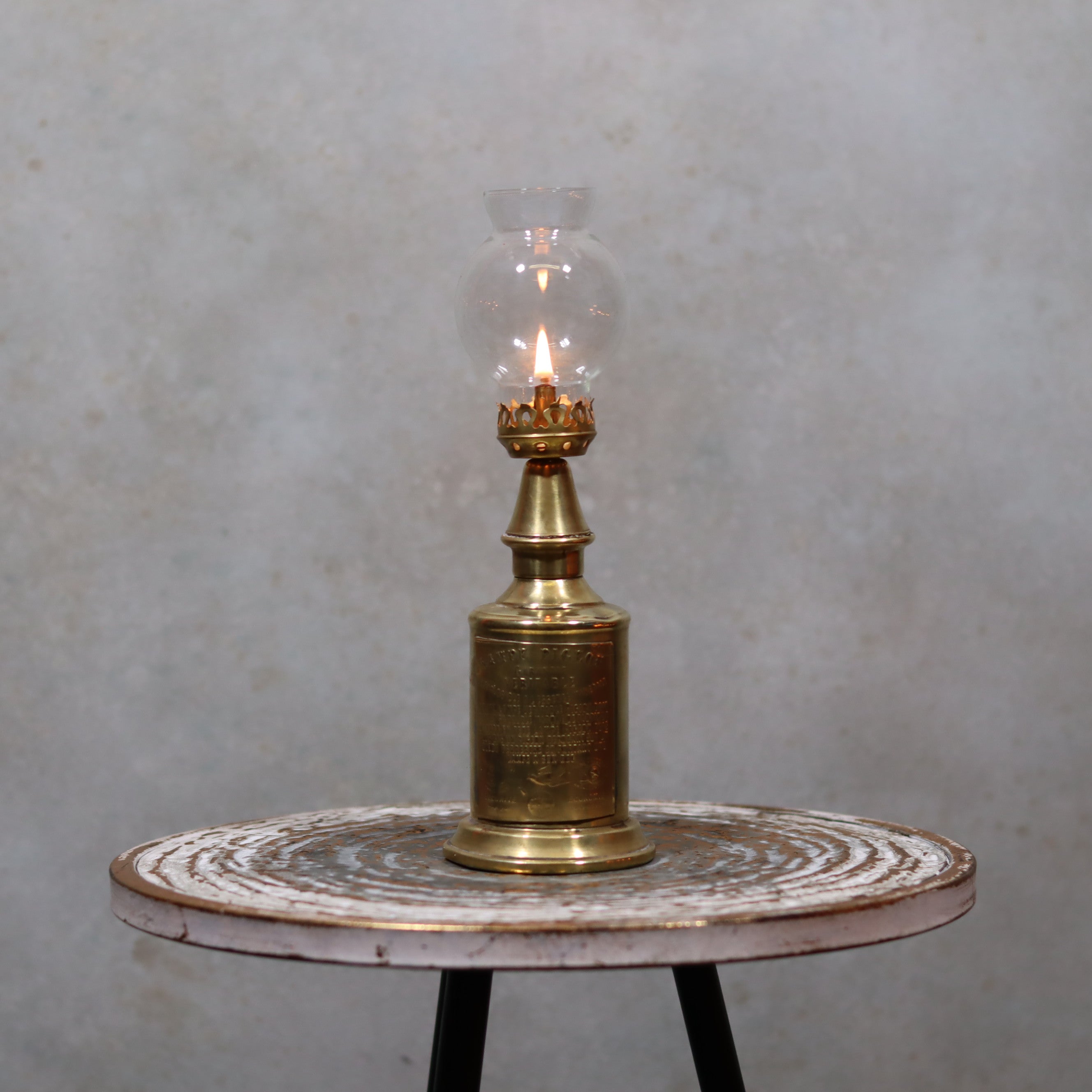 Rare Antique Oil Lamp – Early Pigeon Lamp (Circa 1900) lit on rustic round table against neutral background
