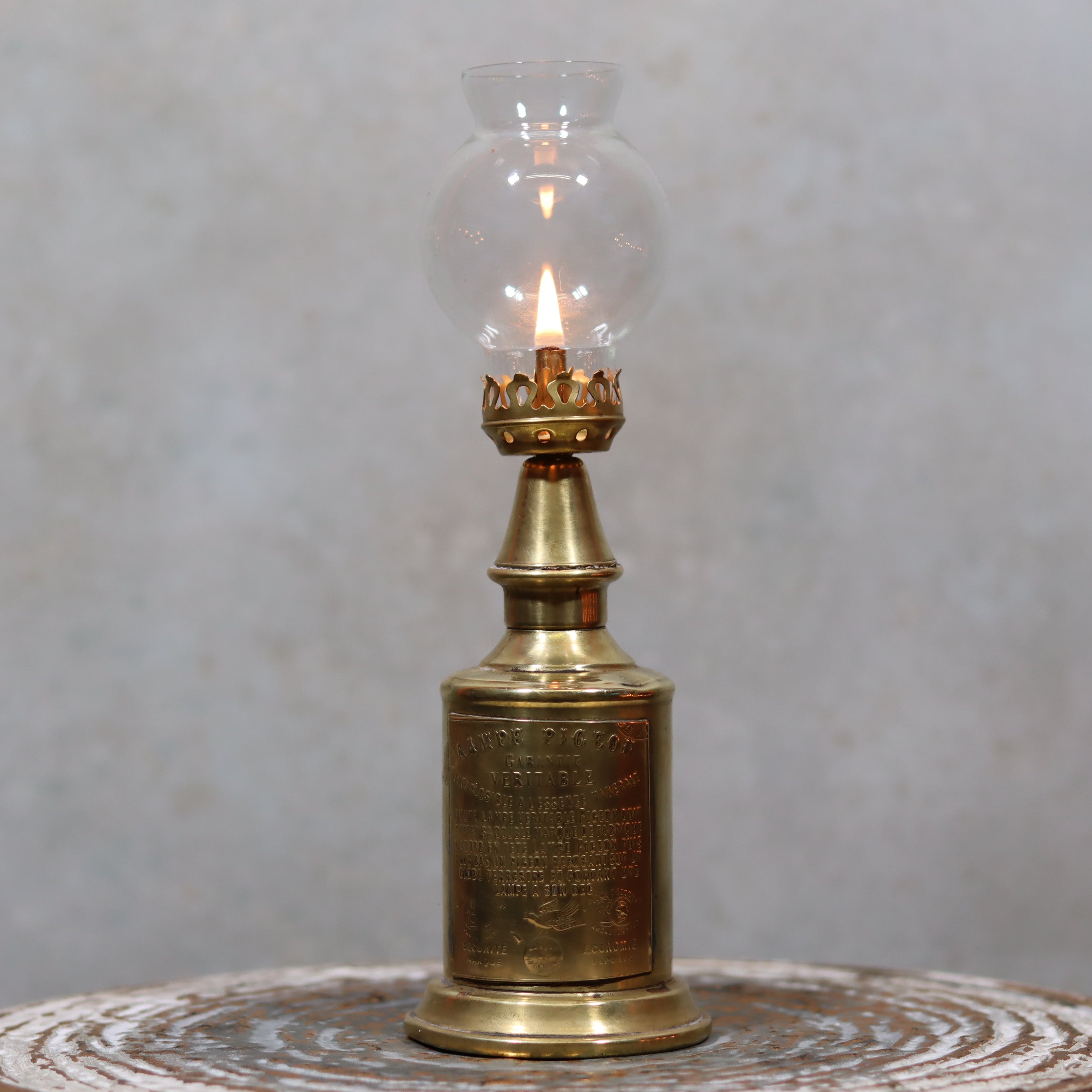 Rare Antique Oil Lamp – Early Pigeon Lamp (Circa 1900) lit with ornate brass and glass design on textured surface