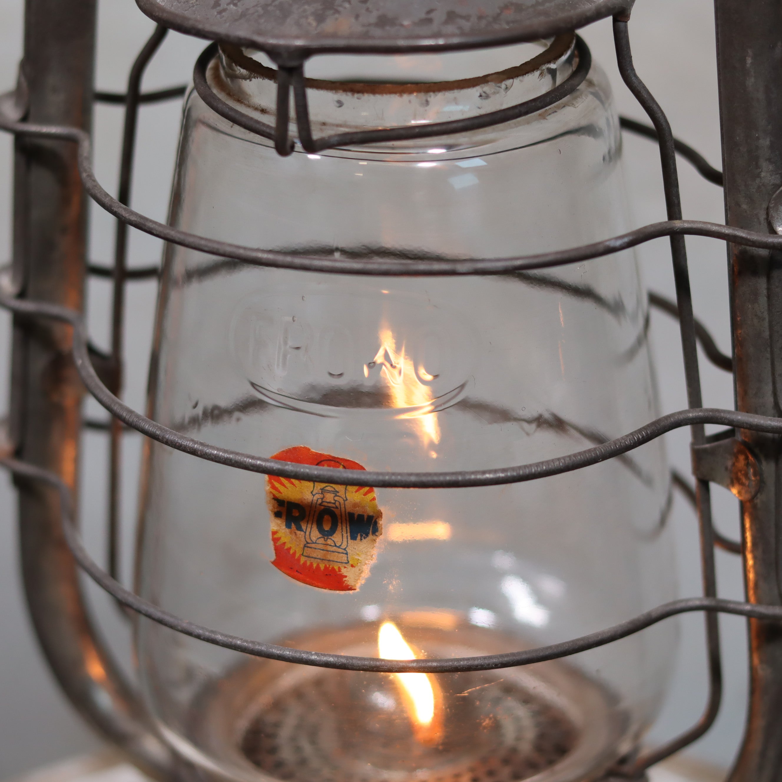 Vintage Frowo 105 Hurricane Lantern – Original Glass & Partial Sticker showing lit oil lamp flame and metal frame close-up.