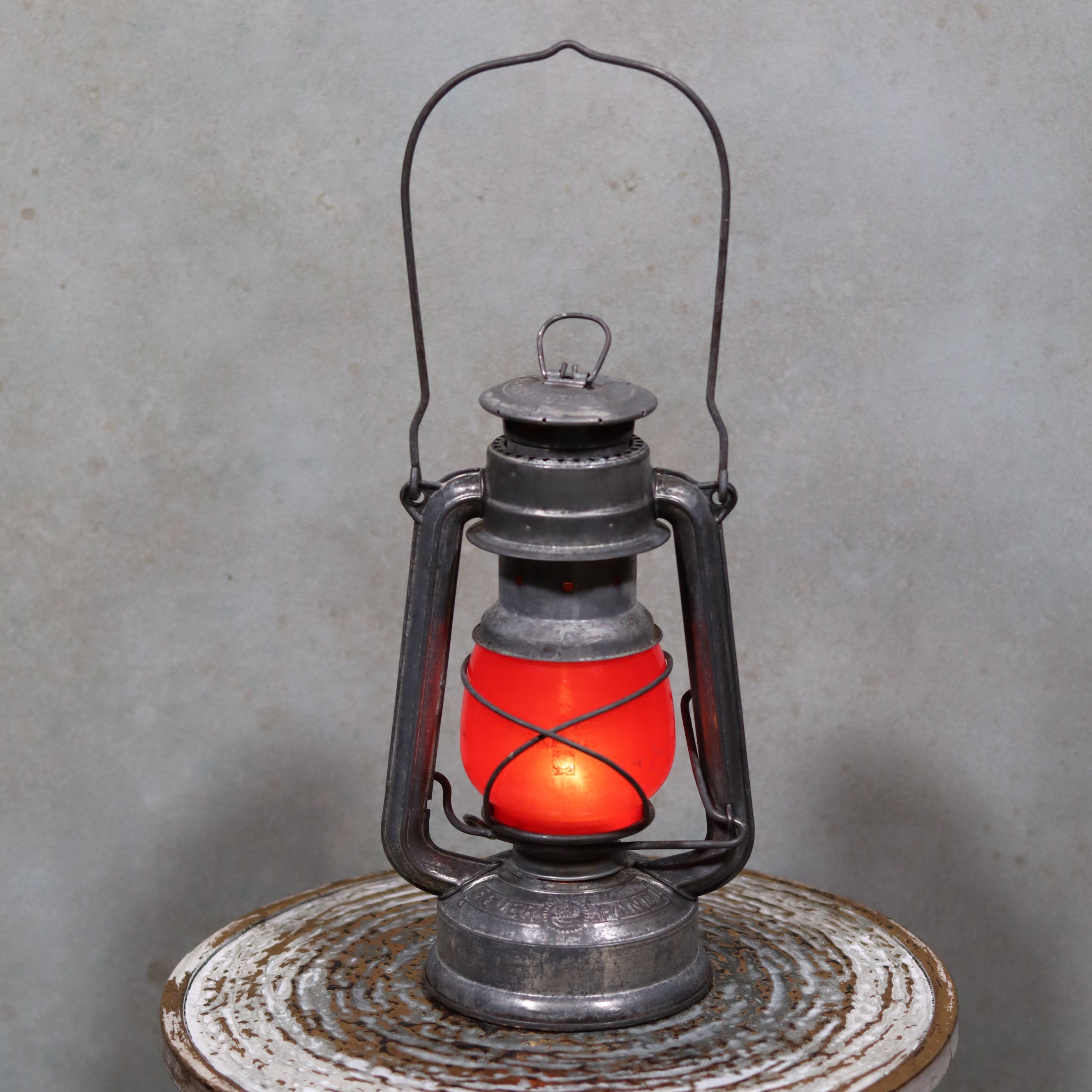 Vintage Feuerhand Baby 275 Hurricane Lantern – Western Germany – Red Glass oil lamp with glowing light on rustic surface