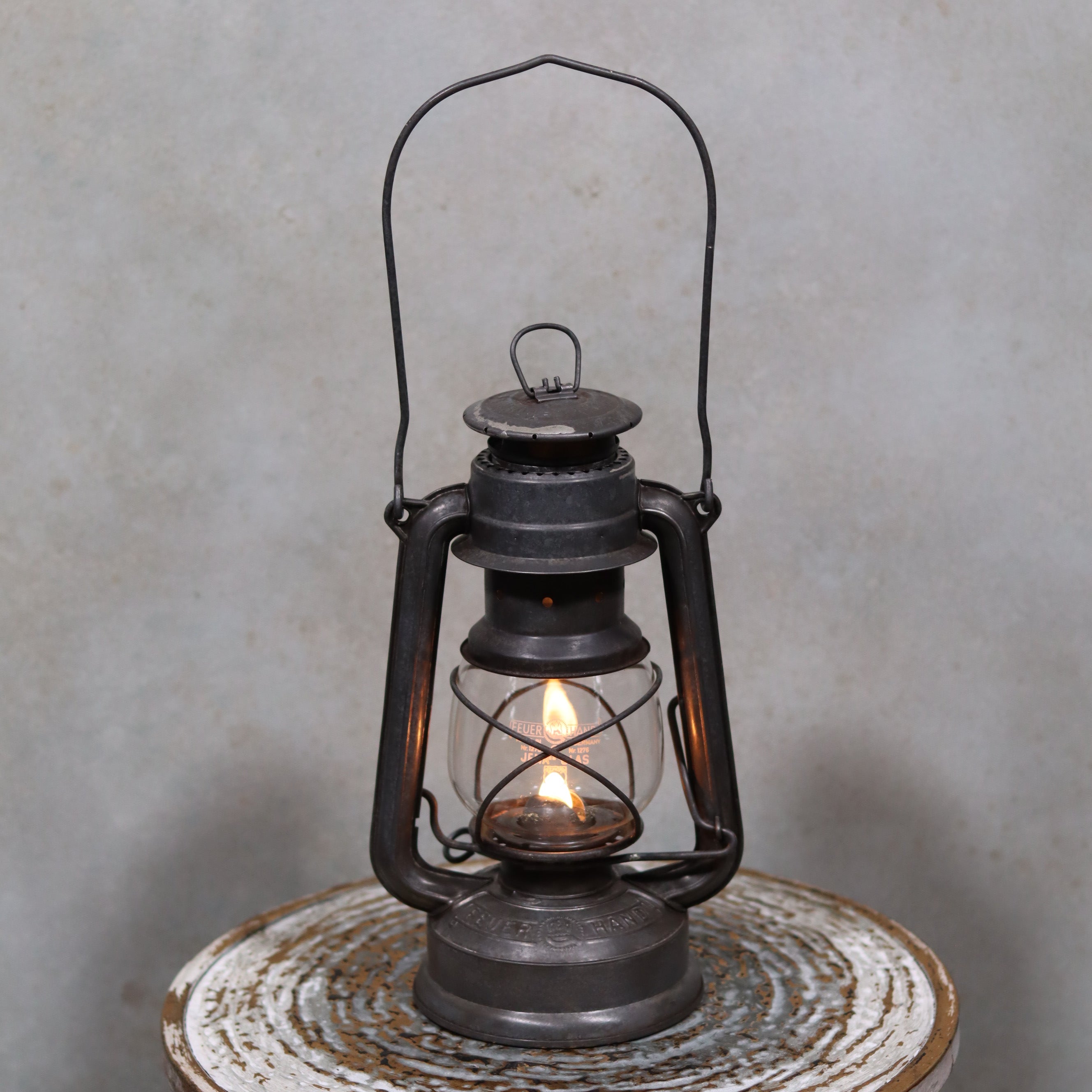Vintage Feuerhand Baby 275 Hurricane Lantern – Western Germany showing lit oil lamp with metal frame and glass enclosure