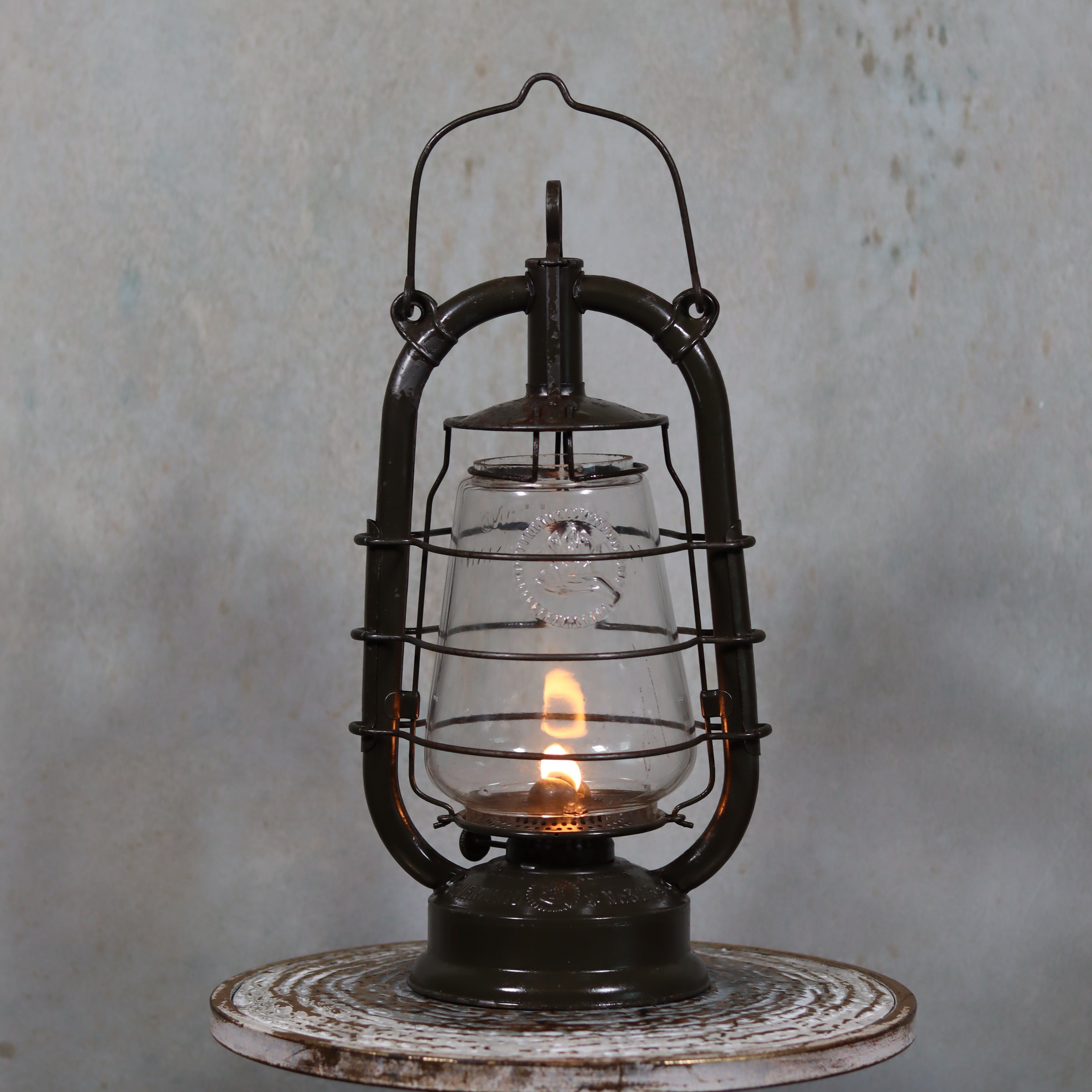 Vintage Feuerhand 323 Storm Lantern – Late 1930s oil lamp with original paint and embossed glass lit on rustic wooden surface