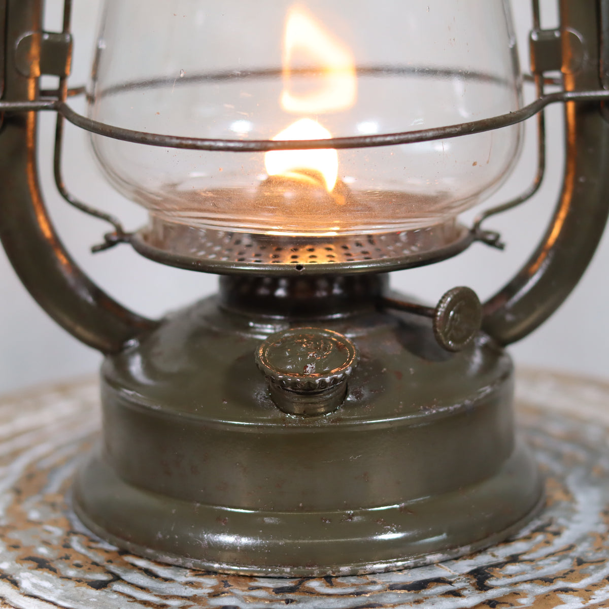 Vintage Feuerhand 323 Storm Lantern – Late 1930s, Original Paint & Embossed Glass oil lamp with lit flame and metal base close-up view
