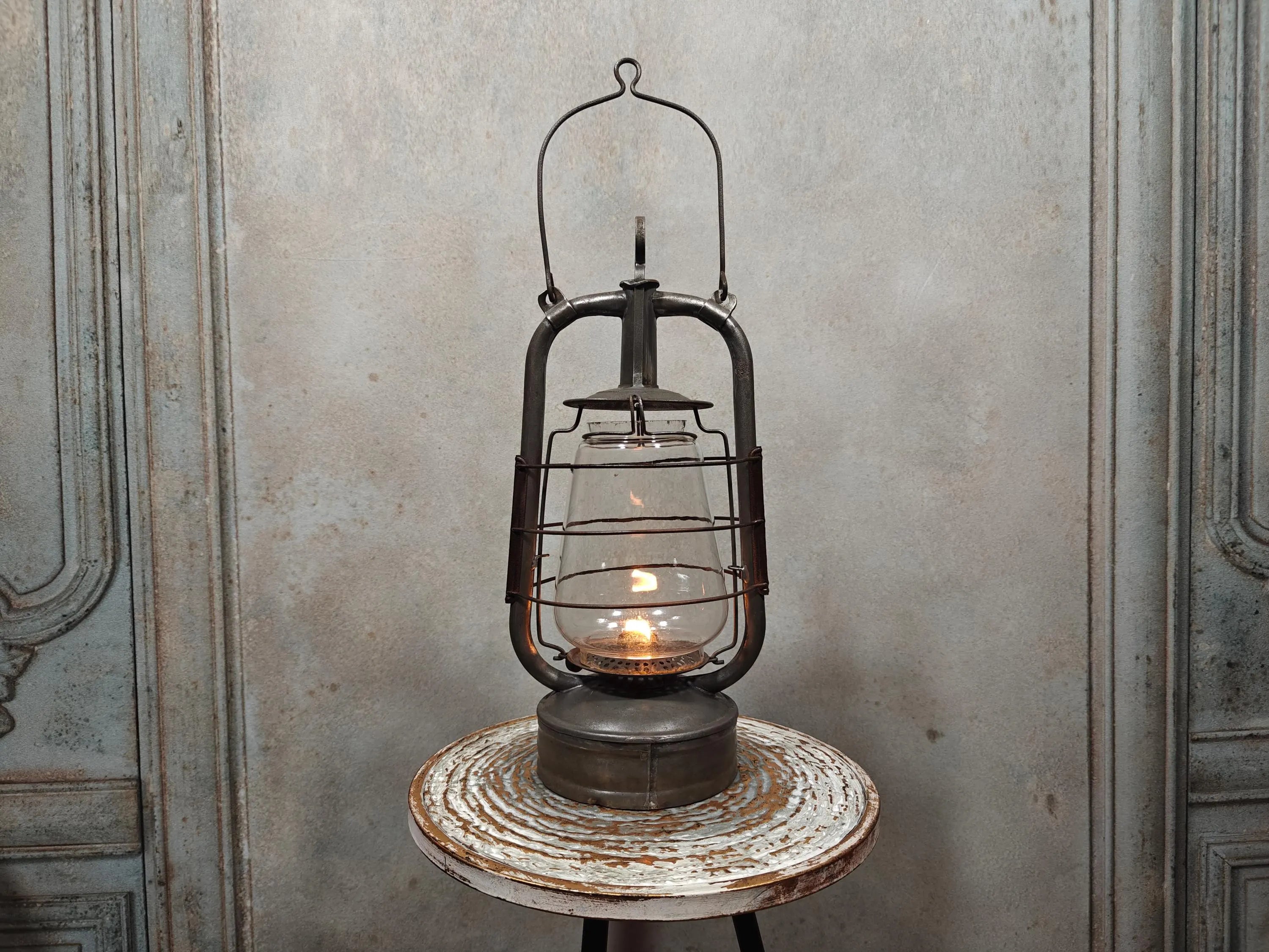 Vintage English Hurricane Lantern – Brass Tank Cap, 1930s Design oil lamp with lit flame on rustic wooden stool.