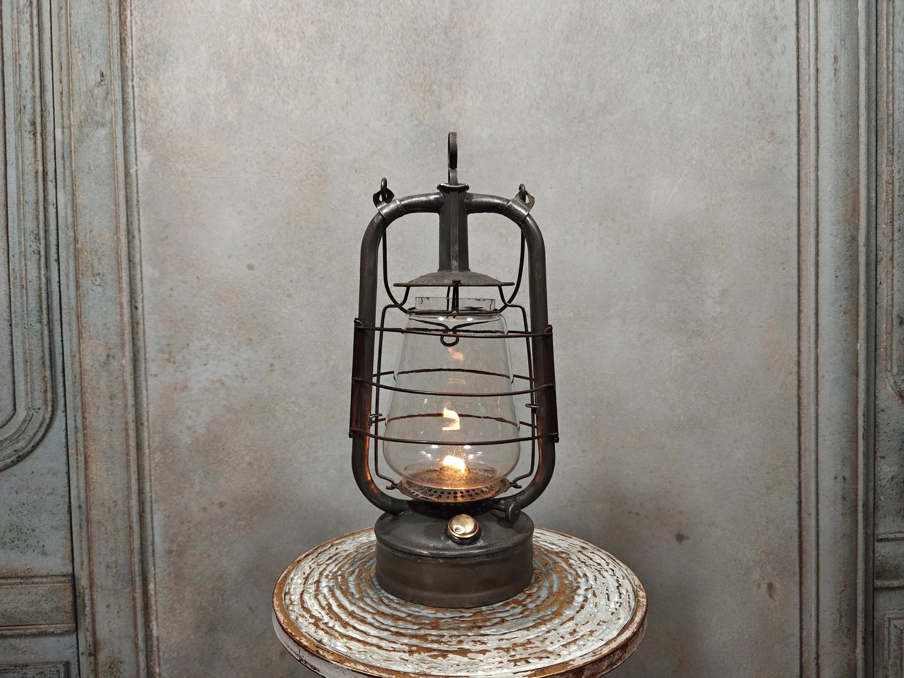 Vintage English Hurricane Lantern – Brass Tank Cap, 1930s Design oil lamp with glowing flame on rustic round table.