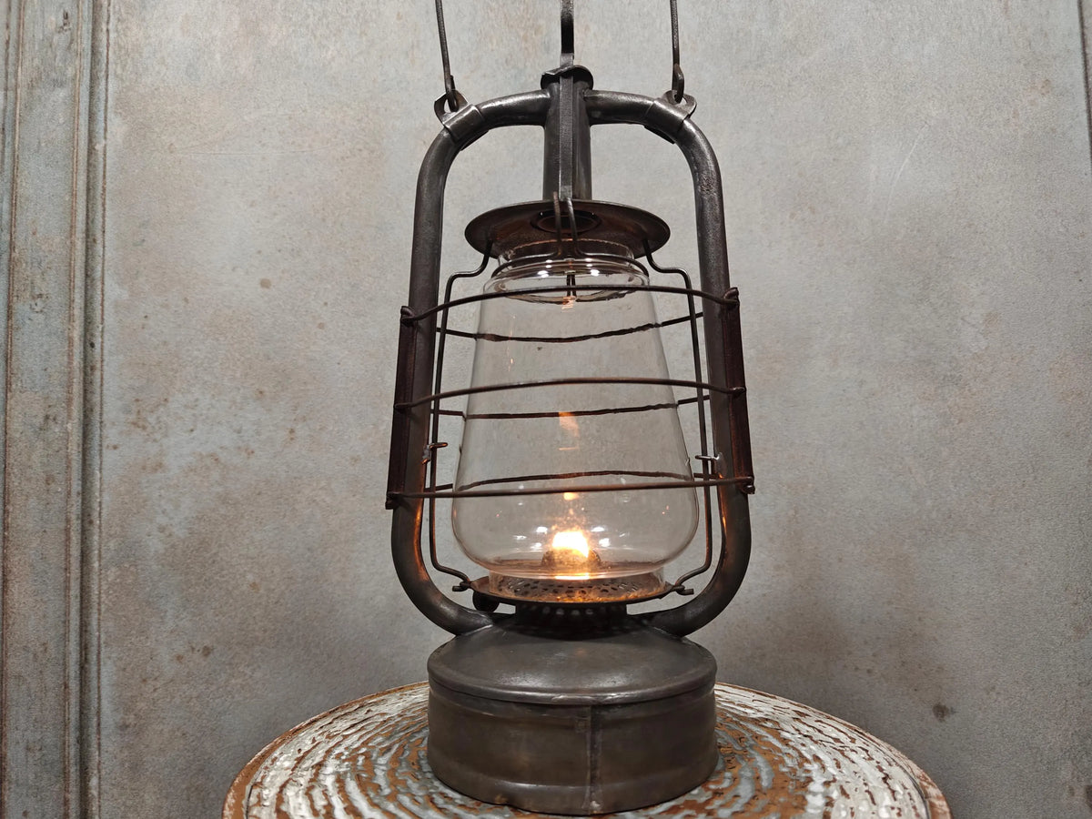 Vintage English Hurricane Lantern – Brass Tank Cap, 1930s Design oil lamp glowing on rustic surface with metal cage protection.