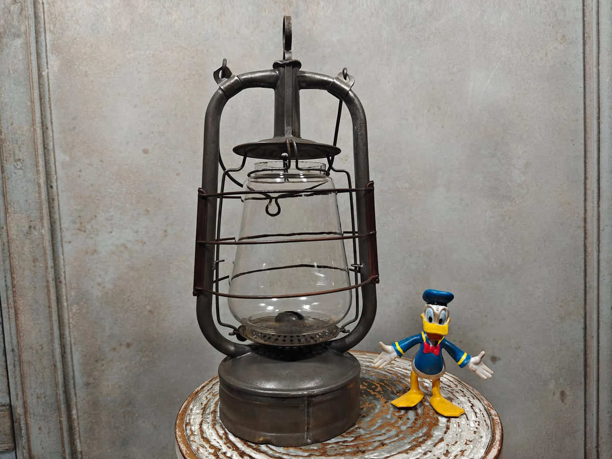 Vintage English Hurricane Lantern – Brass Tank Cap, 1930s Design oil lamp with sturdy metal frame and clear glass globe on rustic surface.